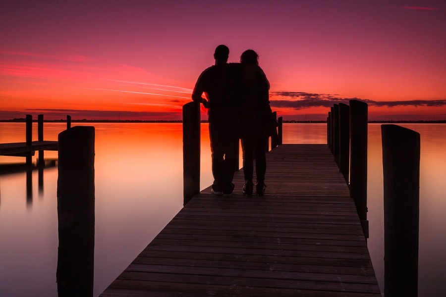 Un muelle de madera que se adentra en aguas tranquilas al atardecer, con un cielo colorido.