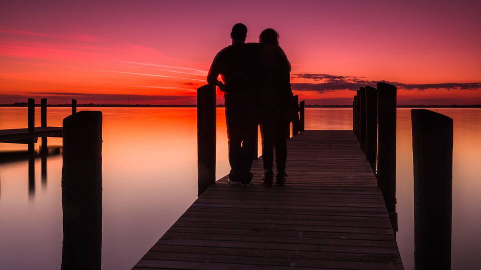 A wooden pier extending into calm water at sunset with a vibrant sky.