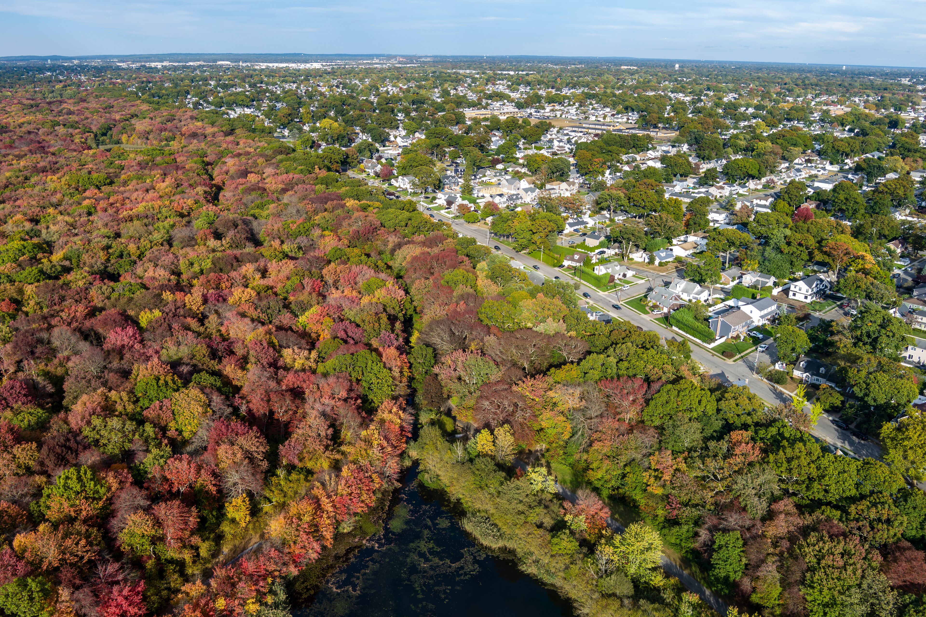 An aerial view of a residential area with a river running through it, surrounded by autumn-colored trees.