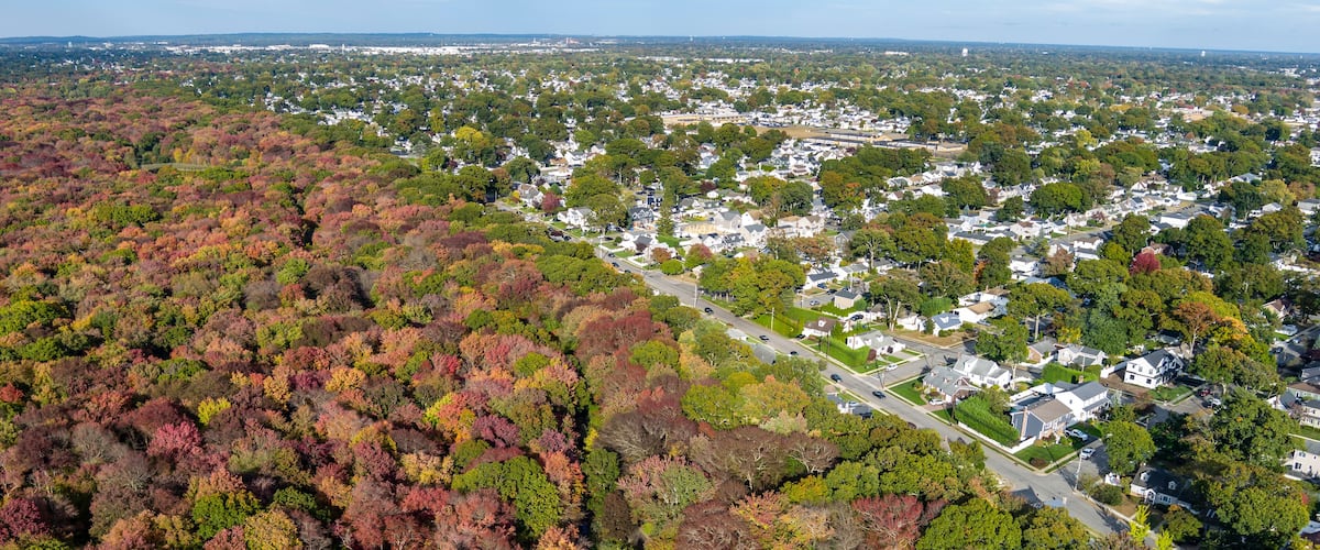 An aerial view of a residential area with a river running through it, surrounded by autumn-colored trees.