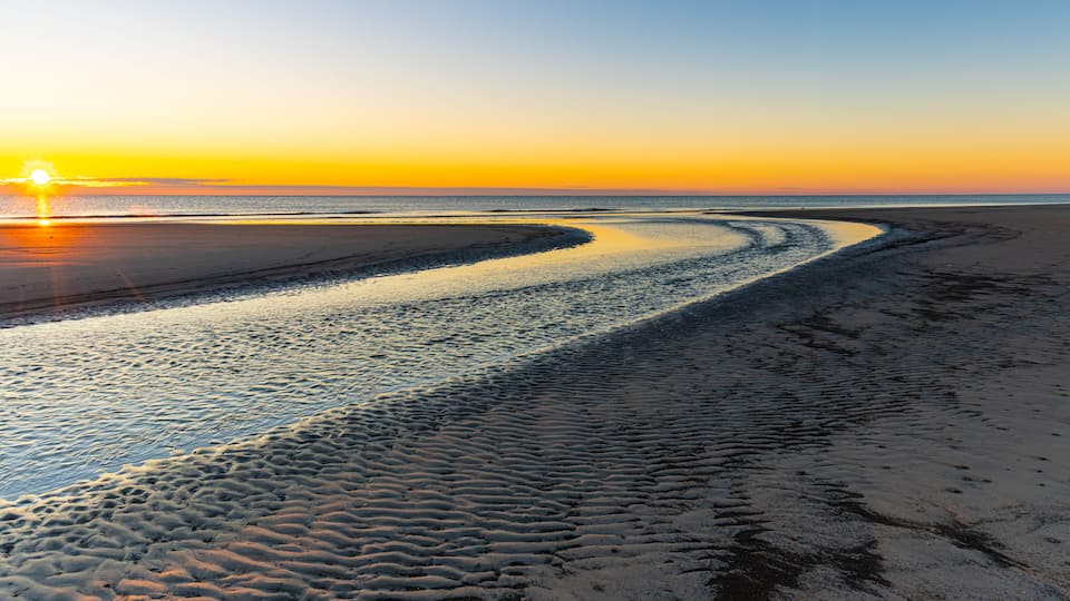 A beach with a curved shoreline and a sunset in the background.