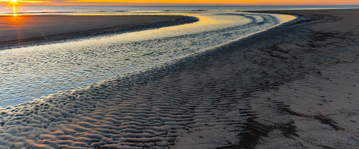 A beach with a curved shoreline and a sunset in the background.