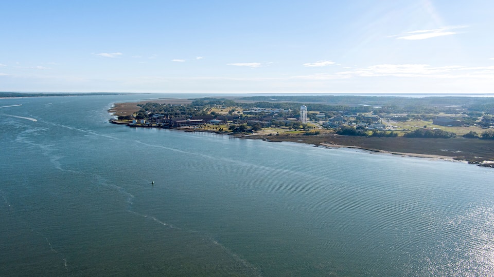 An aerial view of a coastal town with a marina, a lighthouse, and surrounding farmland.