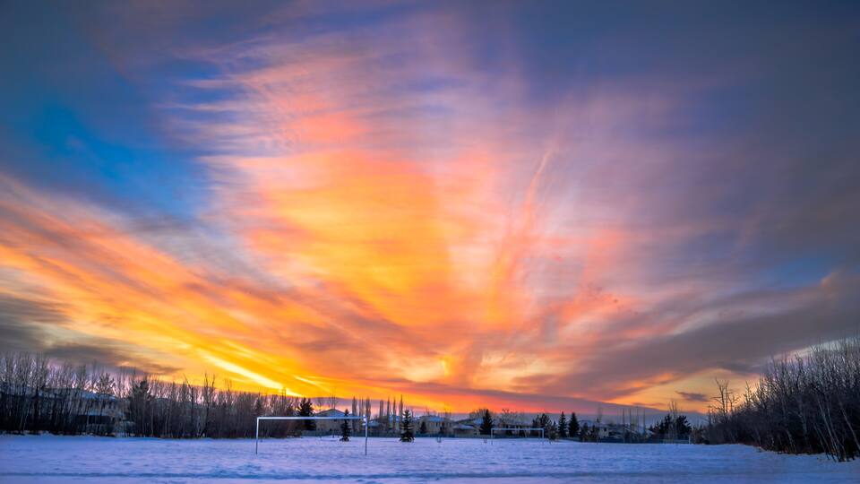 A snowy landscape with a sunset and a soccer field.
