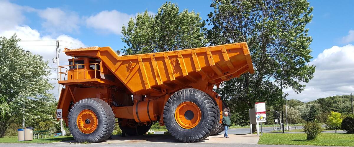 A large orange dump truck parked on a road with trees and a clear sky in the background.