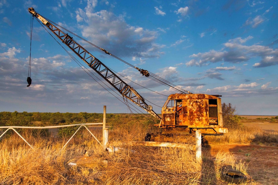 A rusted crane in a dry, grassy field with a clear sky.