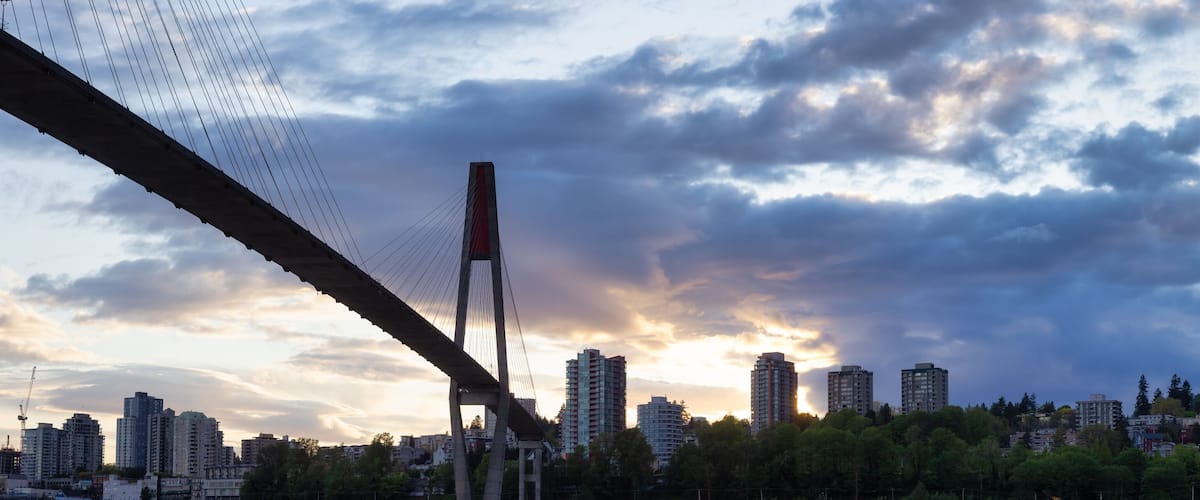 A cityscape with a bridge, tall buildings, and a sunset.