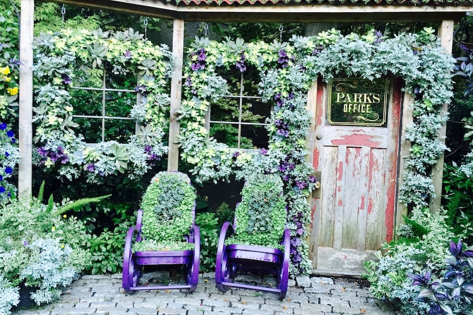 Una porta de fusta amb el rètol 'Parks Office', envoltada de vegetació exuberant i dues cadires morades.