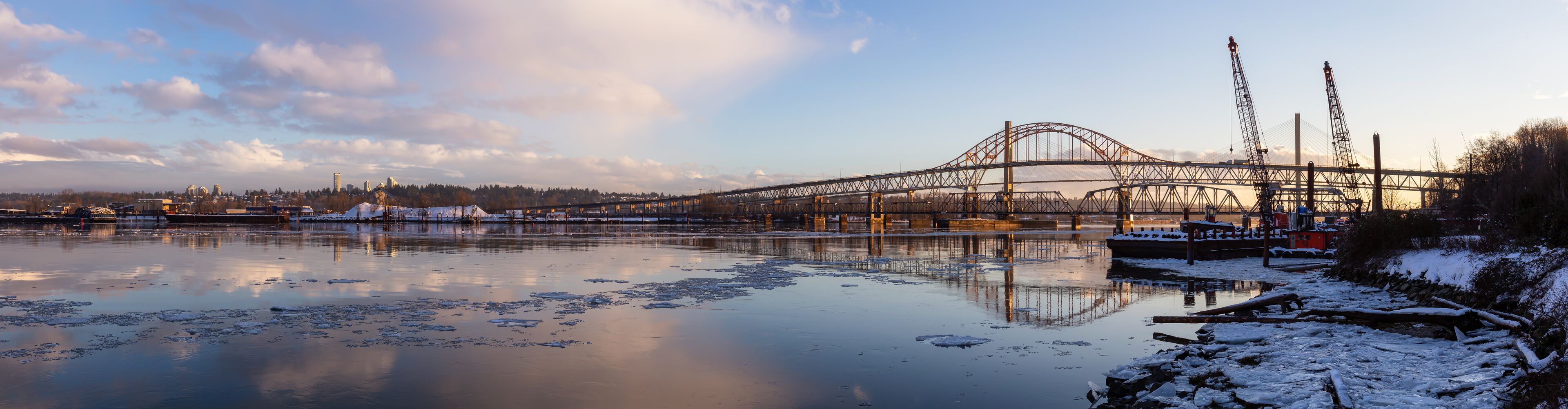 A large bridge spanning a frozen river with snow on the banks.
