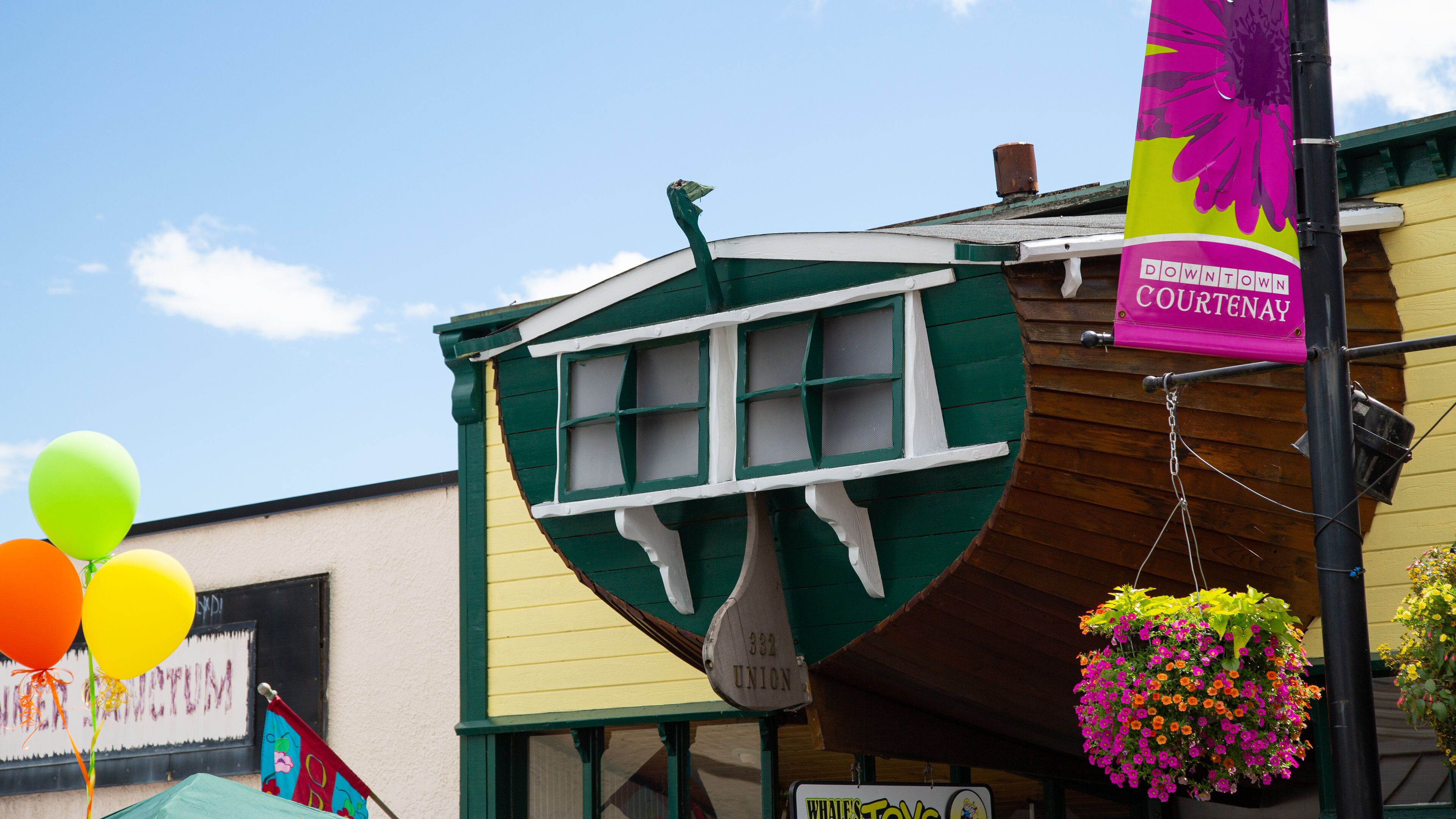 A building with a green and yellow facade, a sign reading "Downtown Courtenay," and a hanging flower basket.