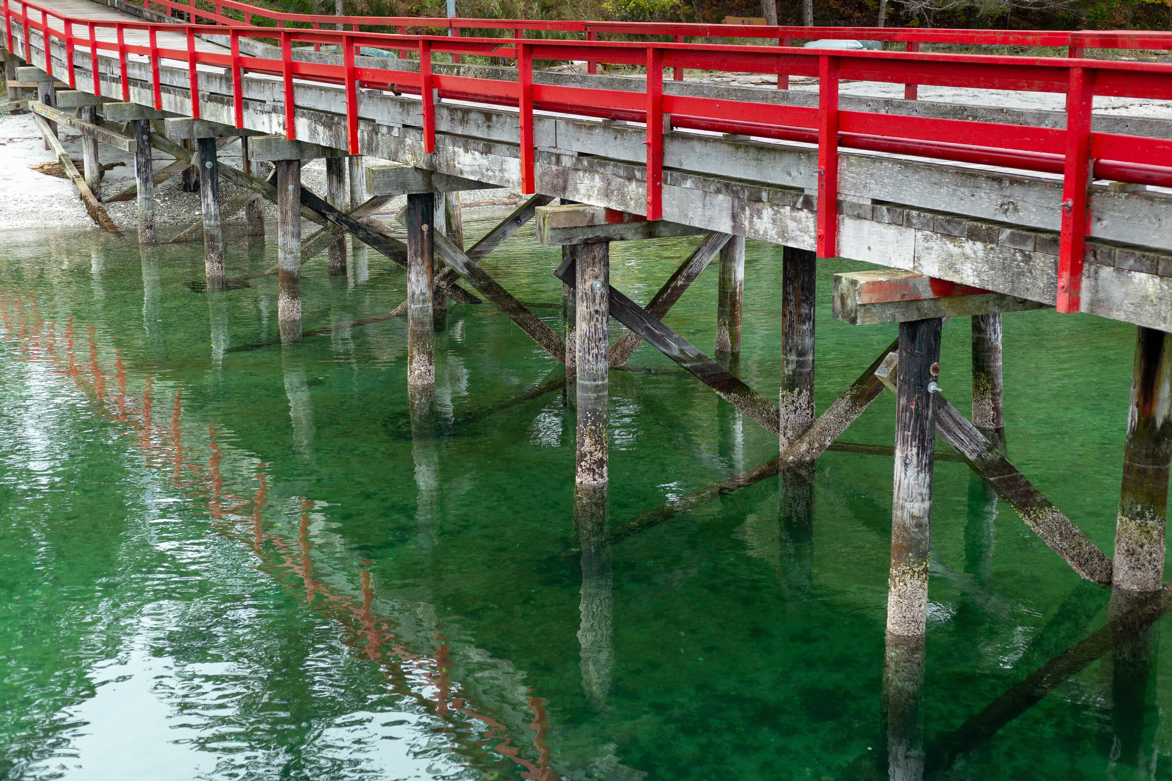 A red bridge over clear green water with wooden supports.