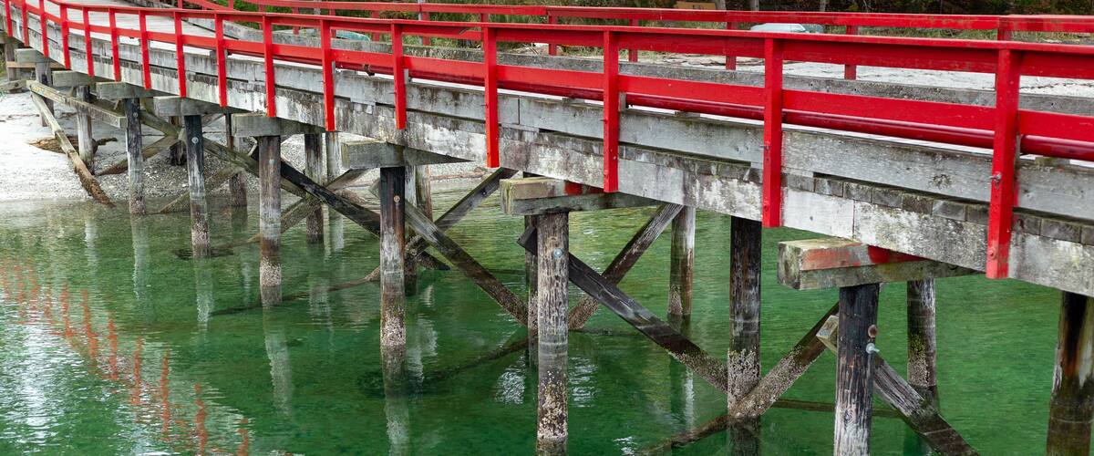 A red bridge over clear green water with wooden supports.