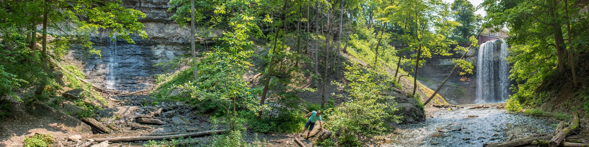 A forested area with a waterfall and a person crossing a stream.