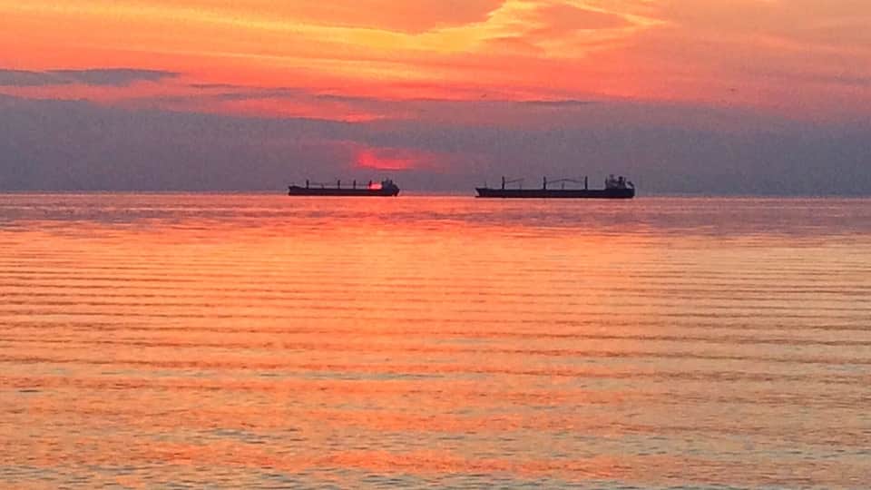 A sunset over a calm sea with two cargo ships.
