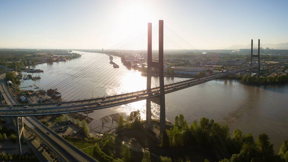 A large suspension bridge spanning a wide river, surrounded by urban areas and greenery.