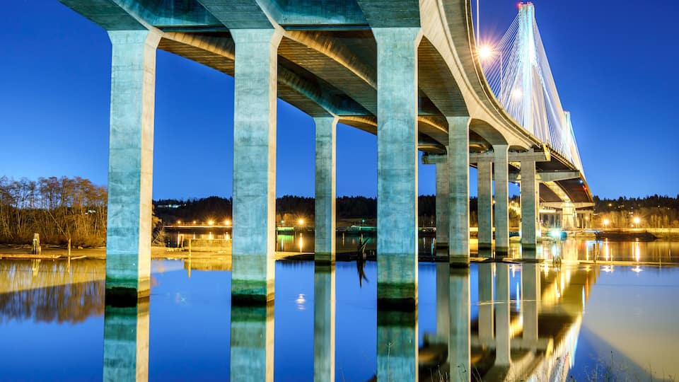 A bridge with illuminated cables at dusk over a calm body of water reflecting the structure.