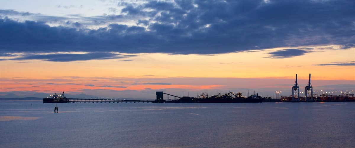 A sunset over a body of water with a bridge and industrial structures in the distance.