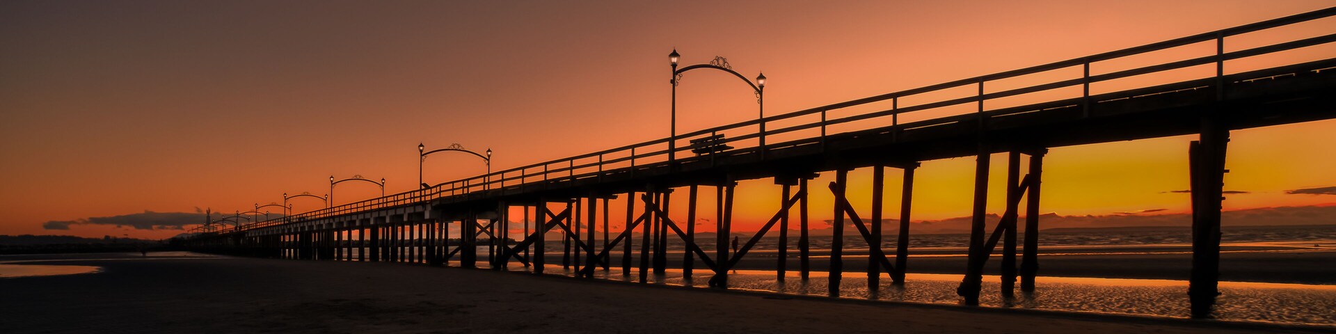 Um píer se estendendo para o oceano ao pôr do sol, com céu claro.