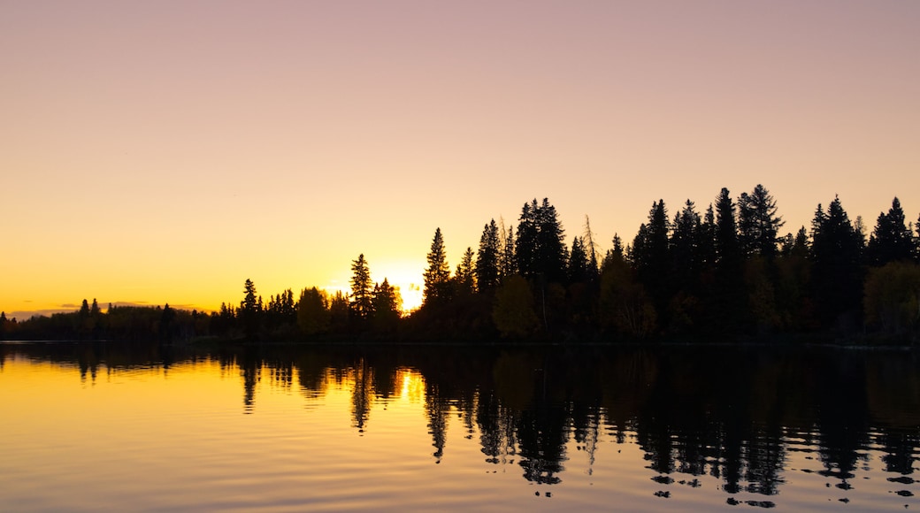 Un lac paisible au coucher du soleil, avec des arbres qui se reflĂštent dans le ciel.