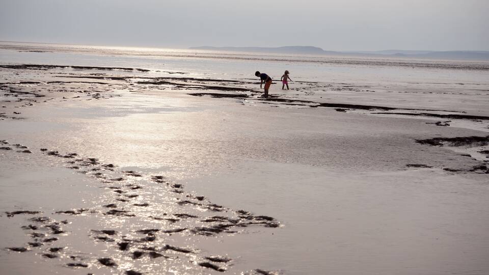 A beach with footprints and two people walking.