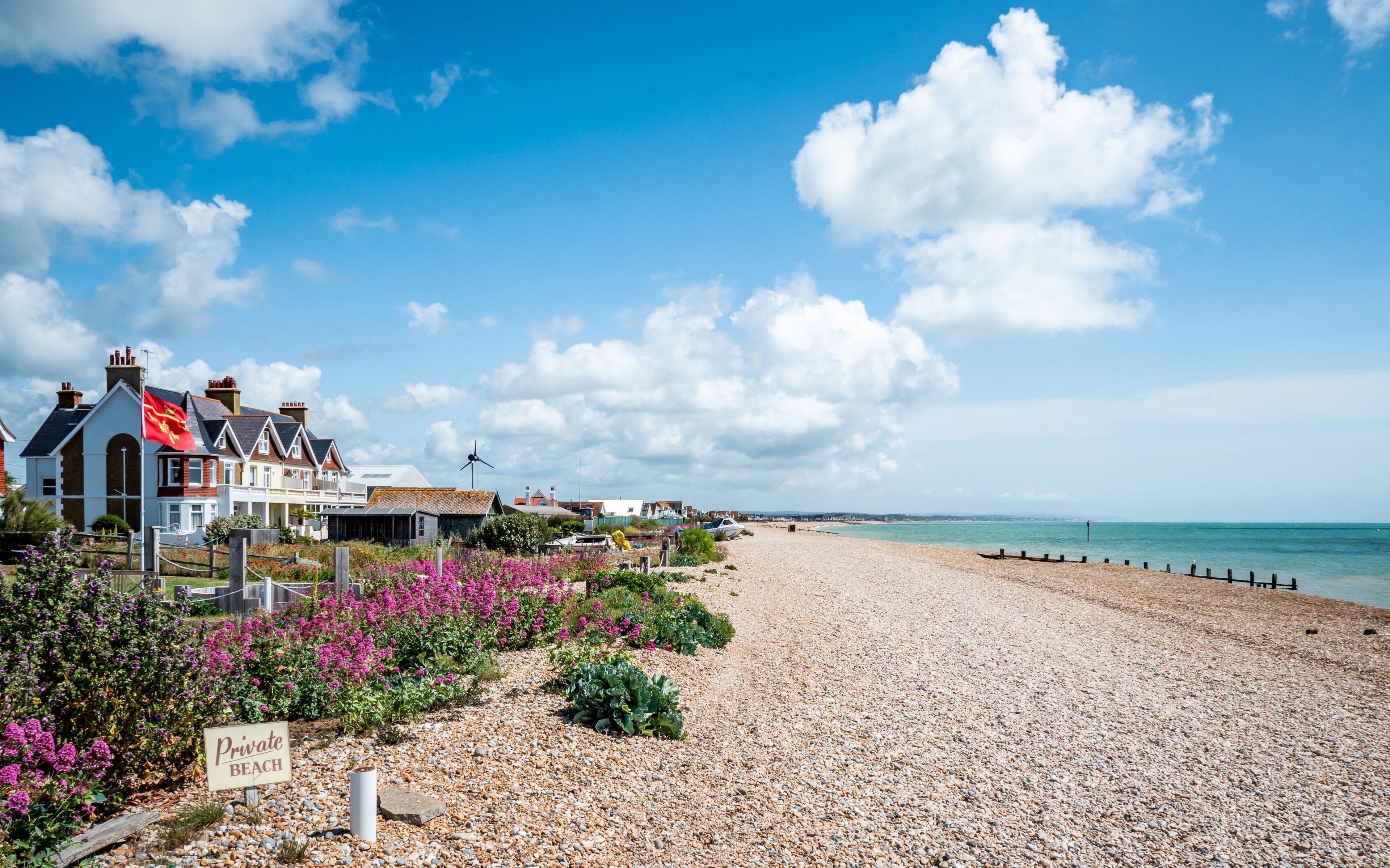 A pebble beach with a flag labeled 'Private Beach,' houses, and a clear blue sky.