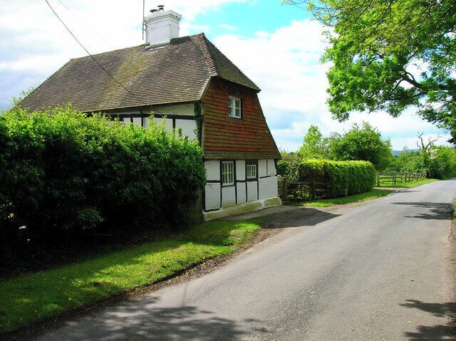 A rural road with a traditional house on the left, surrounded by greenery.