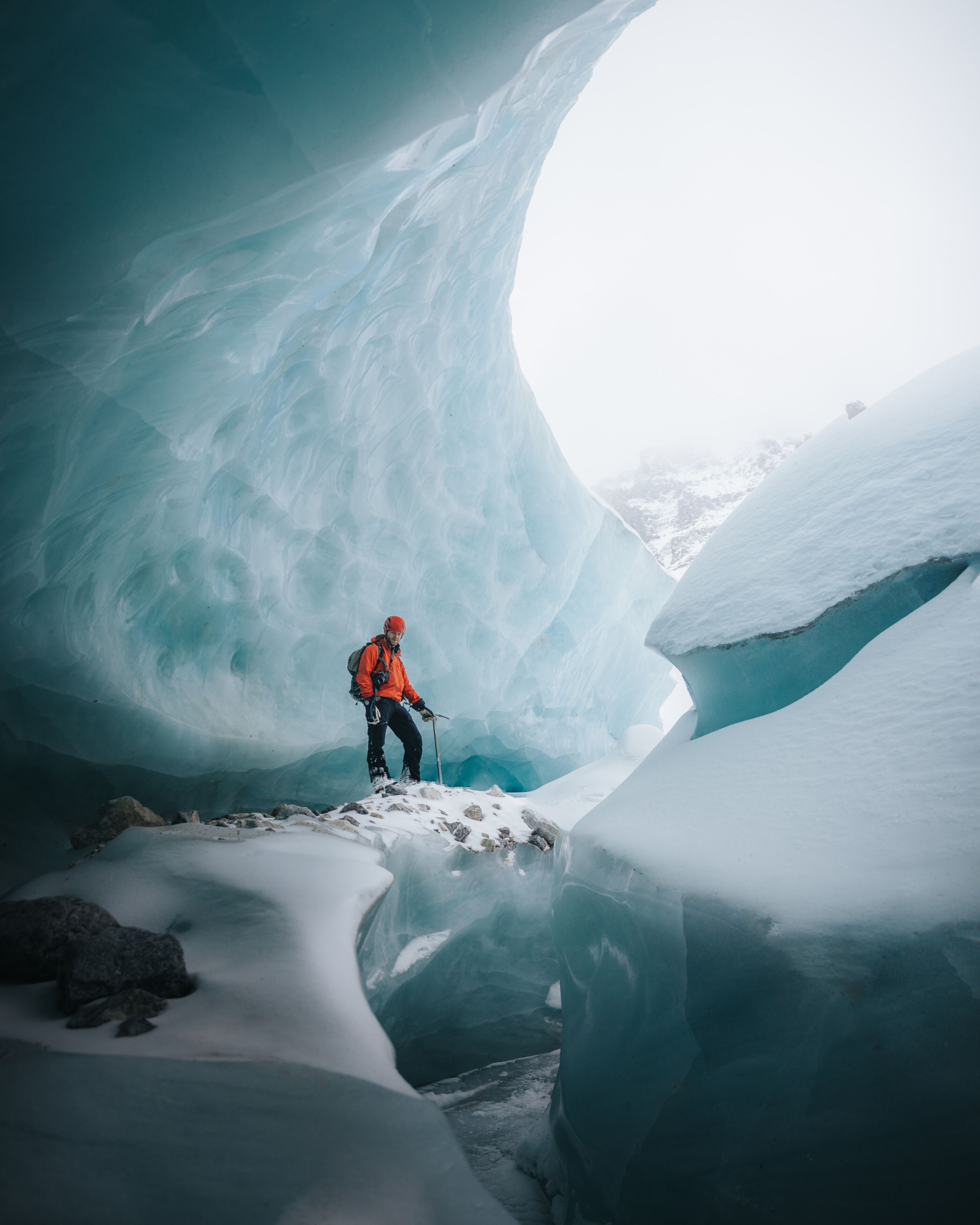 A climber in an ice cave with a large ice arch.