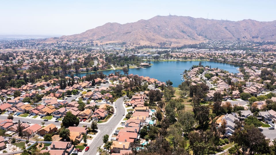 A residential area with houses, roads, and a lake surrounded by mountains.