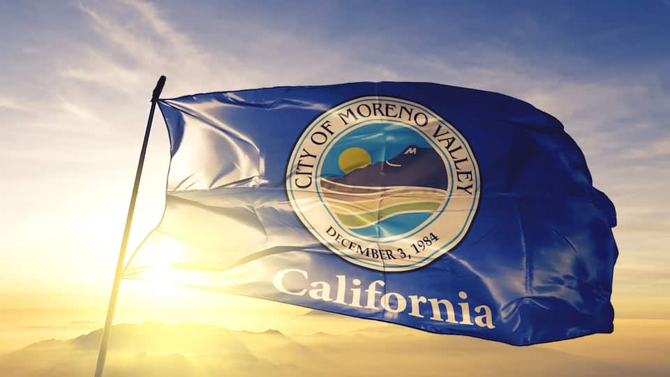 A flag of the City of Moreno Valley, California, with a sunset in the background.
