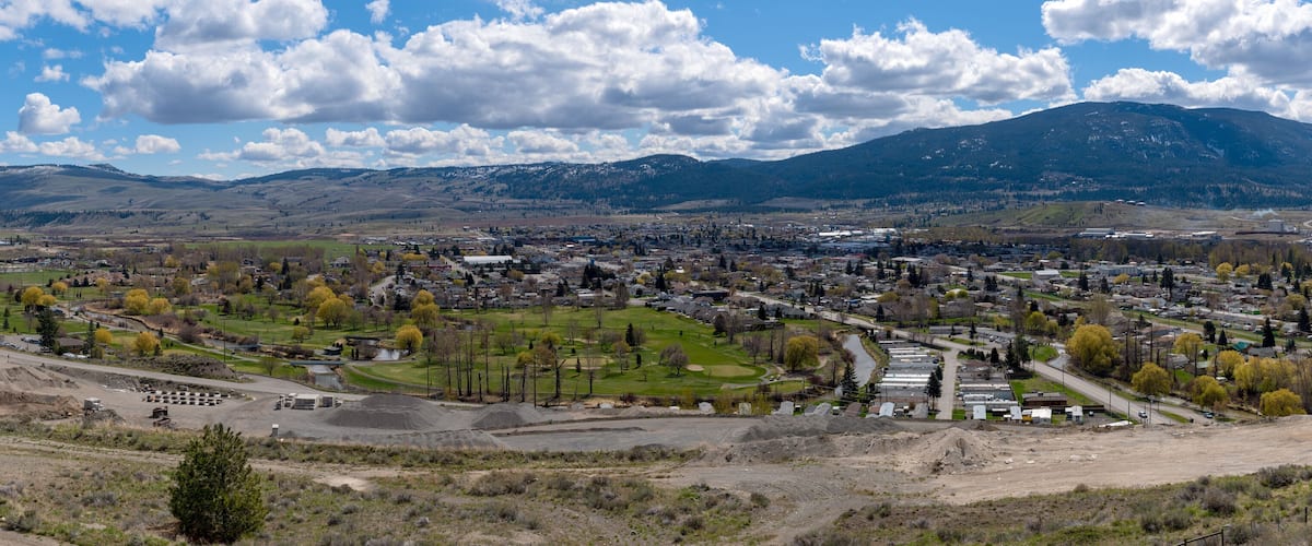 A town with a golf course, a large industrial area, and mountains in the background.