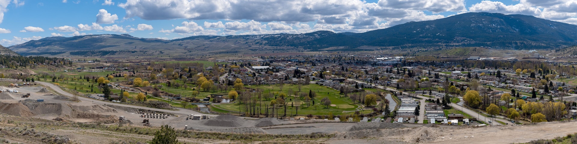 A town with a golf course, a large industrial area, and mountains in the background.