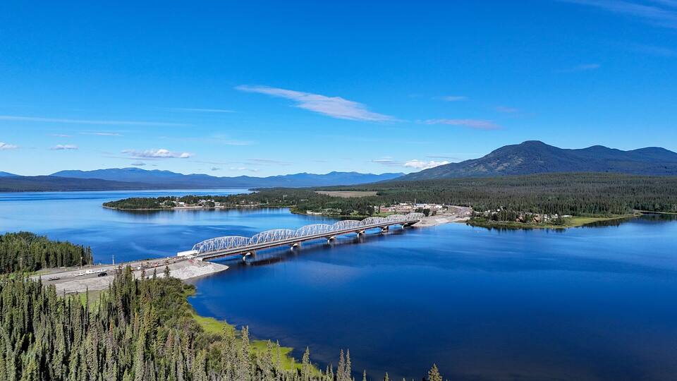 A bridge over a calm lake surrounded by forests and mountains.