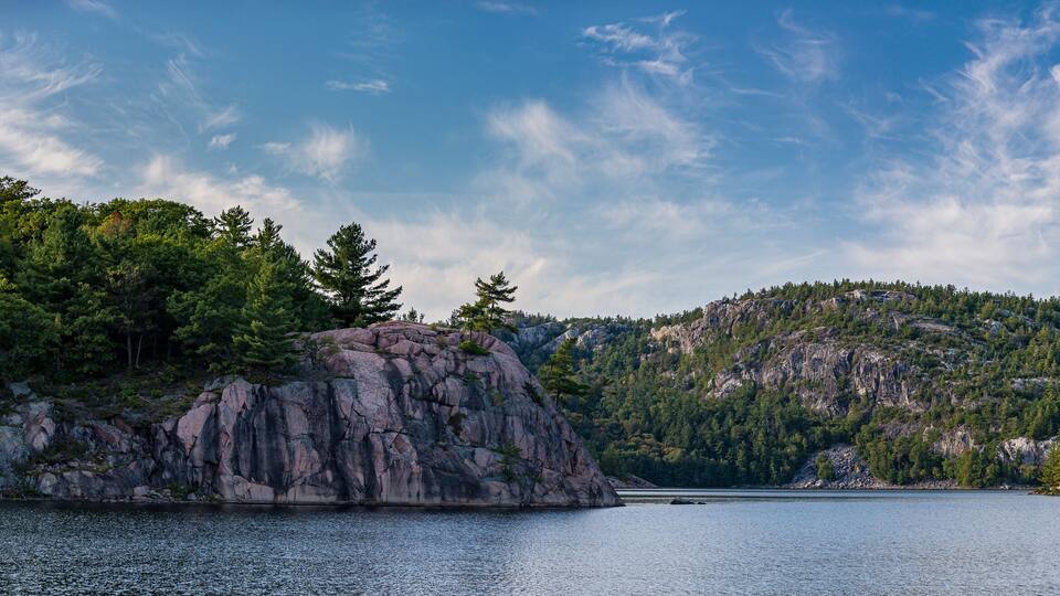 A calm lake surrounded by rocky cliffs and dense forests under a clear sky.