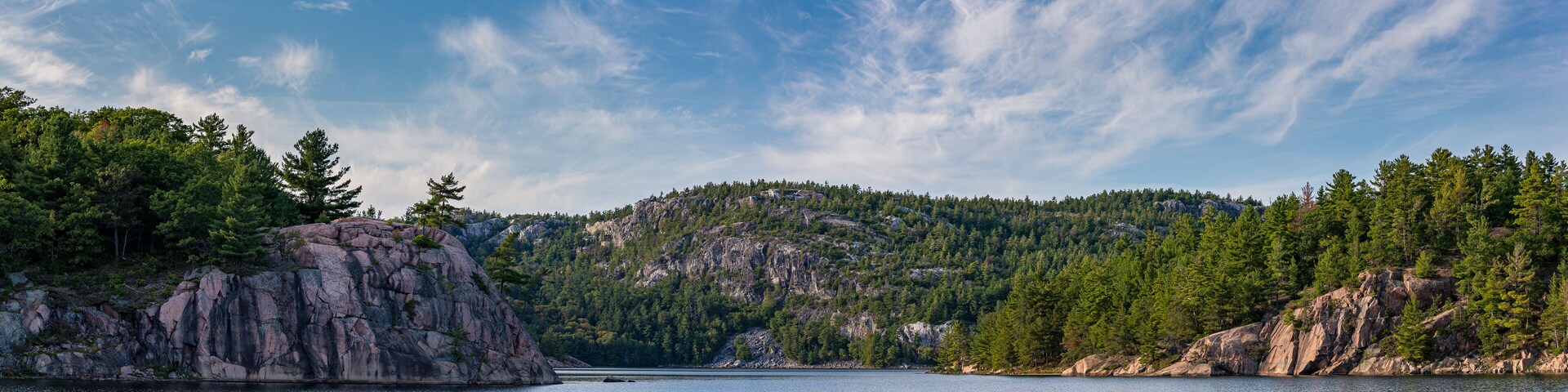 Un lago tranquilo rodeado de riscos y bosques densos bajo un cielo despejado.