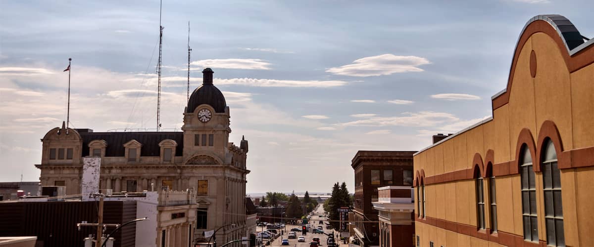 A historic building with a clock tower, a street with cars, and a clear sky with clouds.