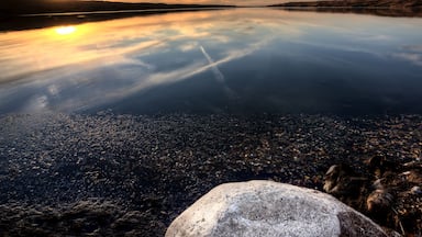 Un lago tranquilo al atardecer con un reflejo claro del cielo, rodeado de terreno rocoso.