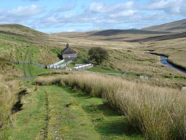 A rural landscape with a small house surrounded by grassy fields and a stream.