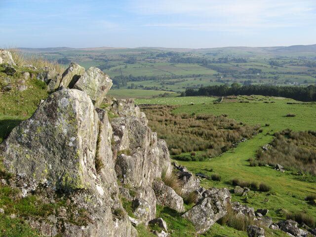 A rocky outcrop with a view of rolling hills and fields.