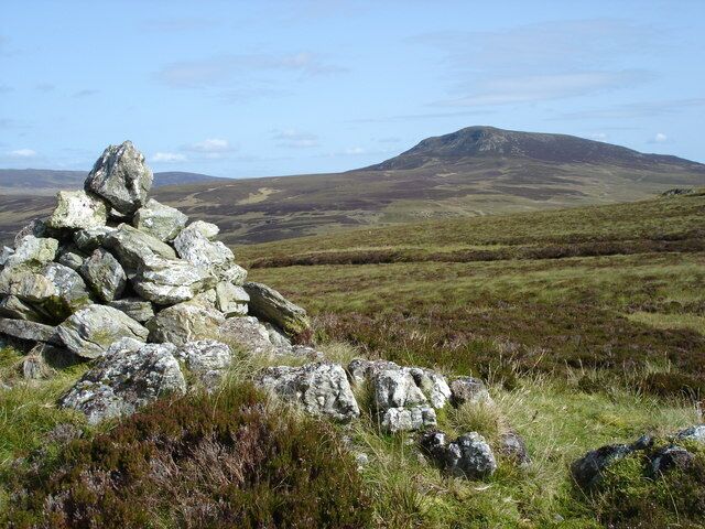 A stone cairn in a grassy field with a mountain in the background.