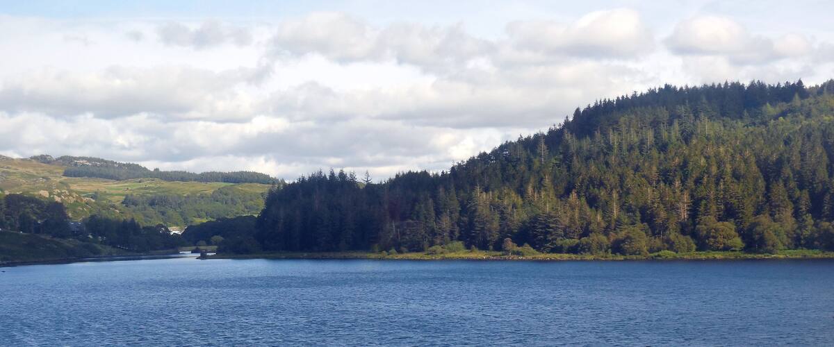 A lake surrounded by forested hills and a small house on the shore.
