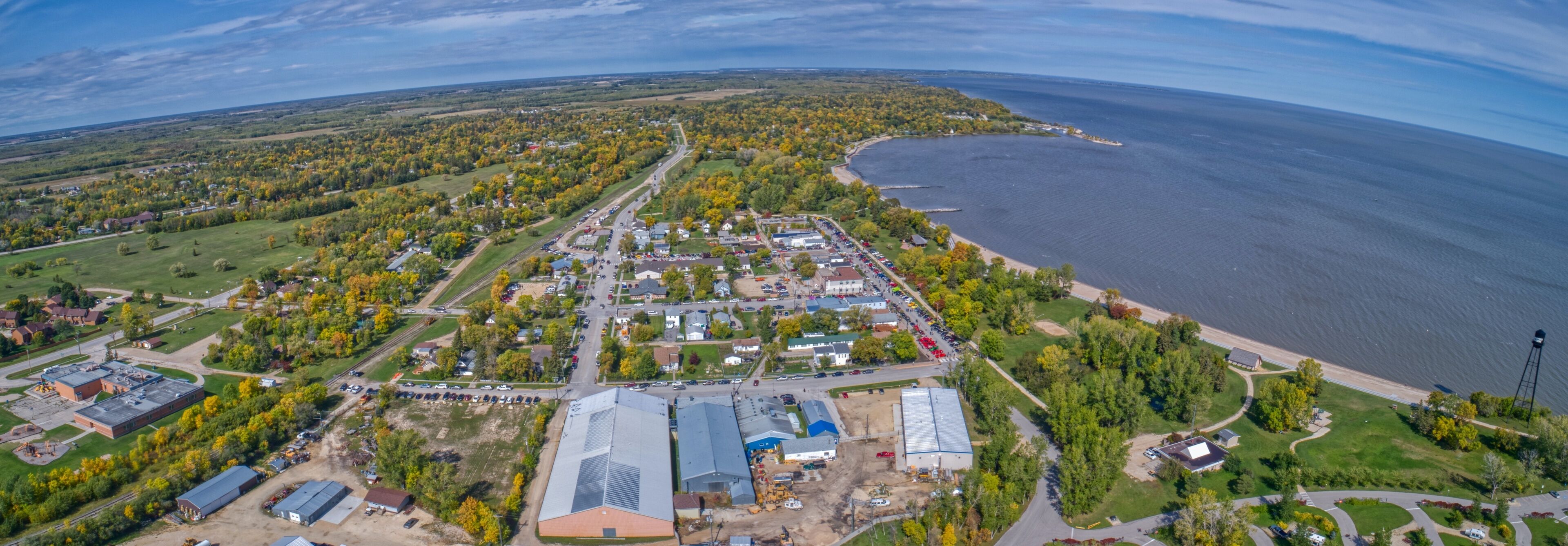 An aerial view of a coastal town with a marina, dense forest, and a large industrial area.