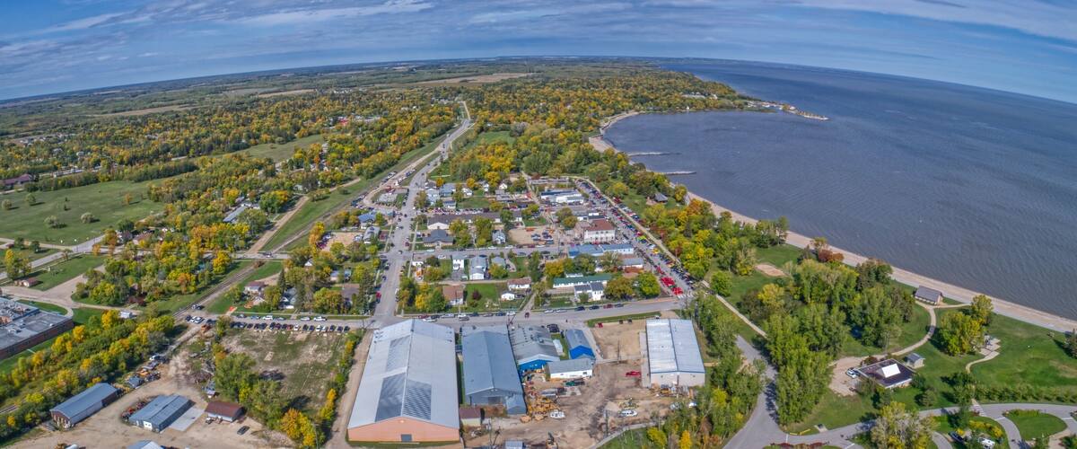 An aerial view of a coastal town with a marina, dense forest, and a large industrial area.