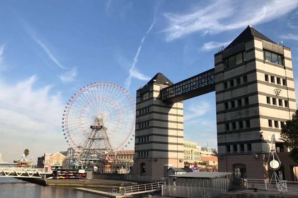 A waterfront with a Ferris wheel, a modern building, and a bridge.