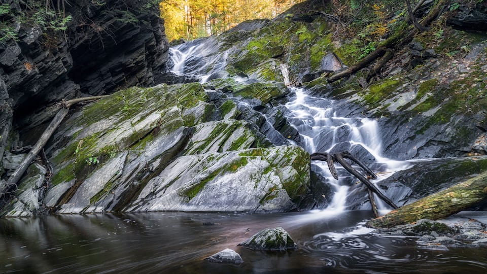 A waterfall cascading over moss-covered rocks in a forested area.