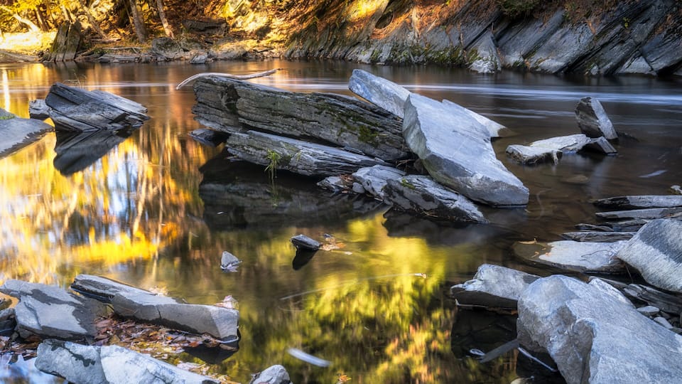 A calm river with large rocks and autumn foliage.