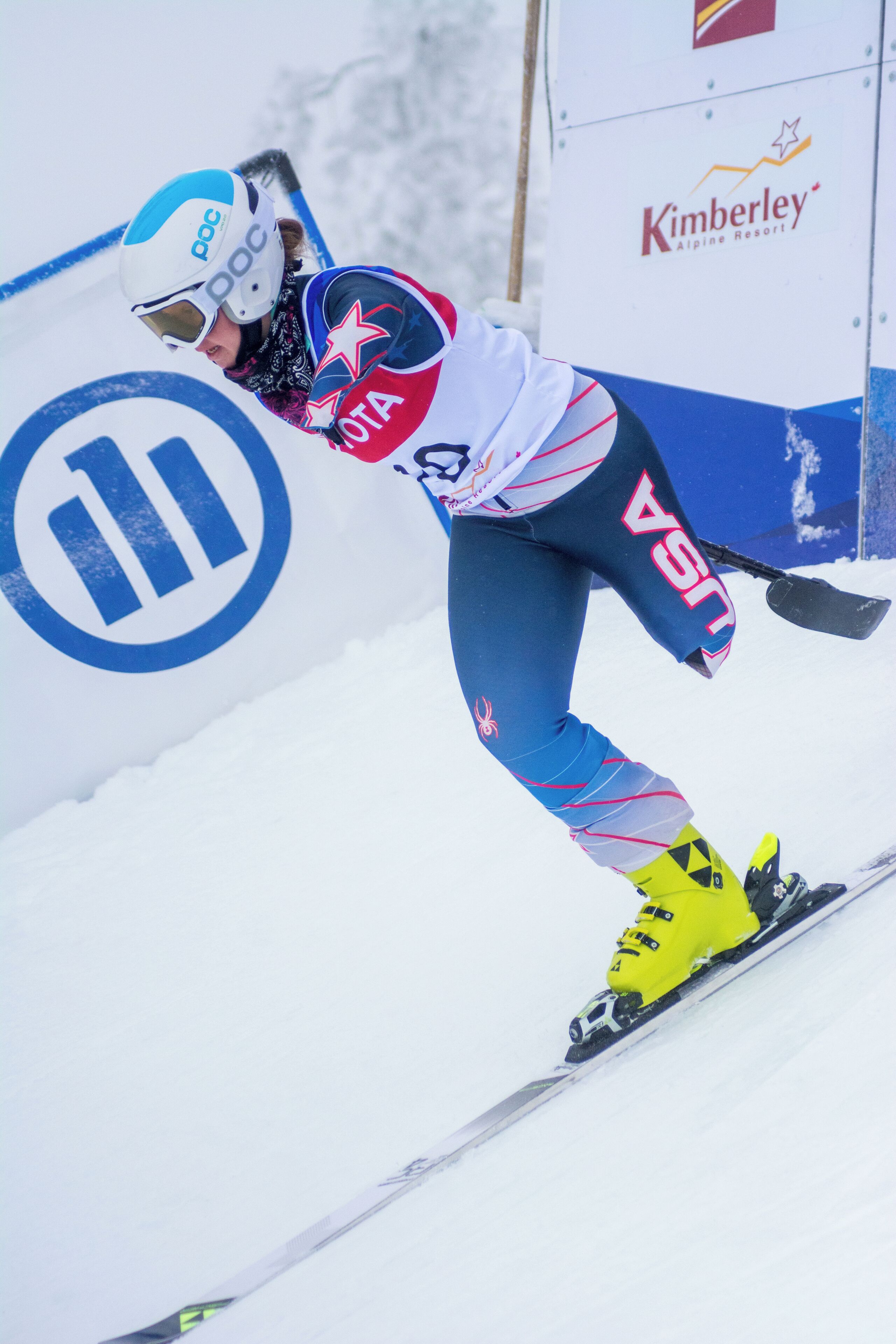 A skier in a blue and white uniform with yellow boots, leaning into a turn on a snowy slope.