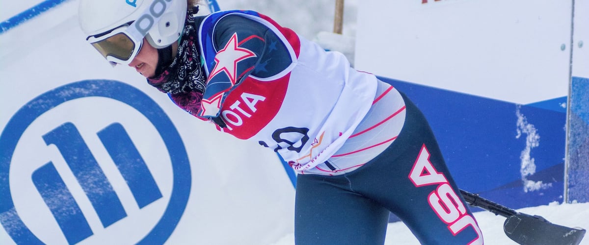 A skier in a blue and white uniform with yellow boots, leaning into a turn on a snowy slope.