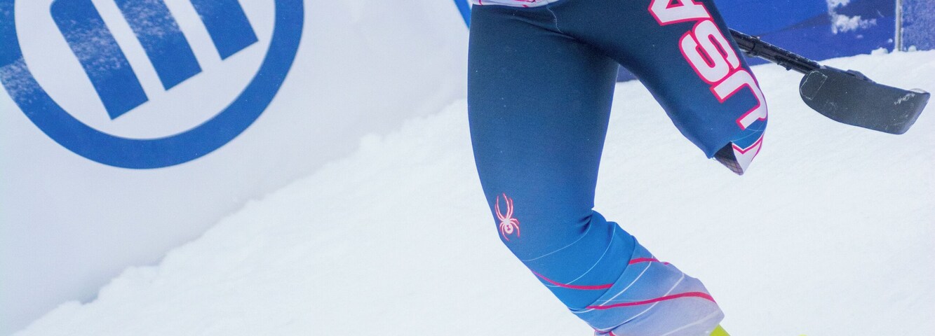 Un esquiador con uniforme azul y blanco y botas amarillas, inclinándose al tomar una curva en una pendiente nevada.