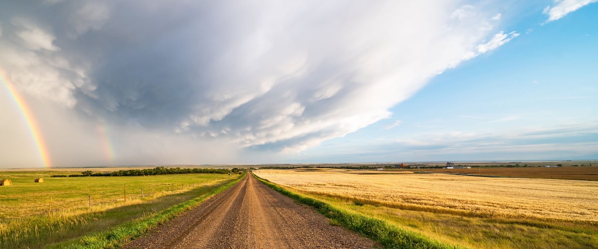 A rural landscape with a dirt road, hay bales, and a rainbow.