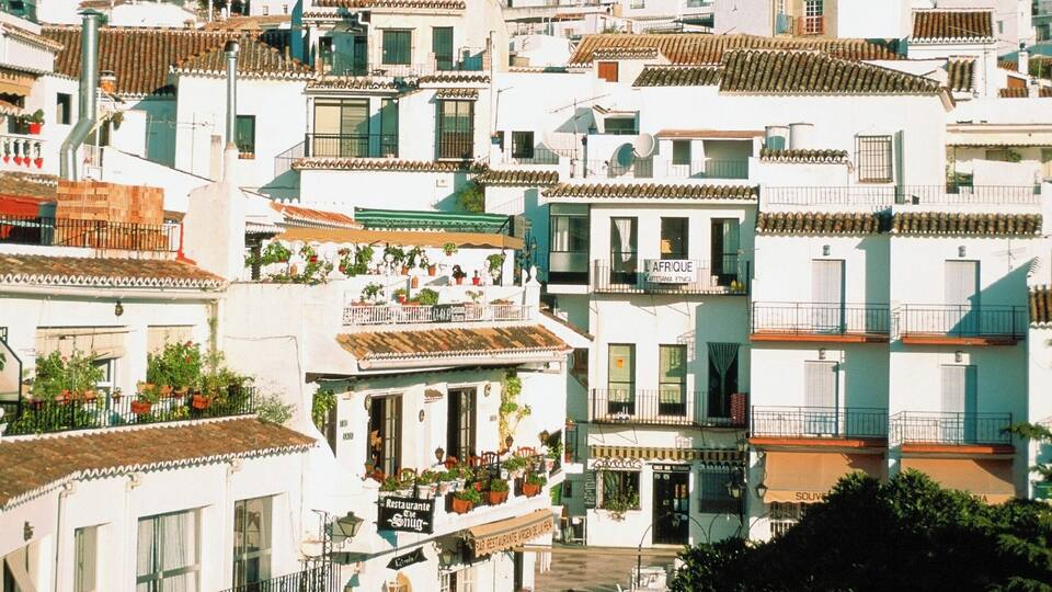 A hillside town with white buildings, a café, and a mountain in the background.